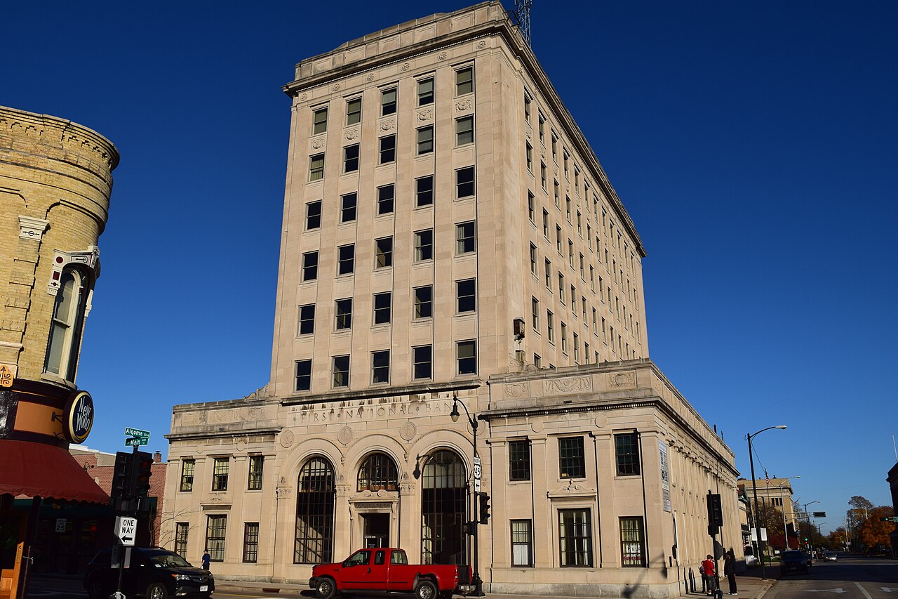 The First National Bank building in downtown Oshkosh, Wisconsin, under a clear blue sky.